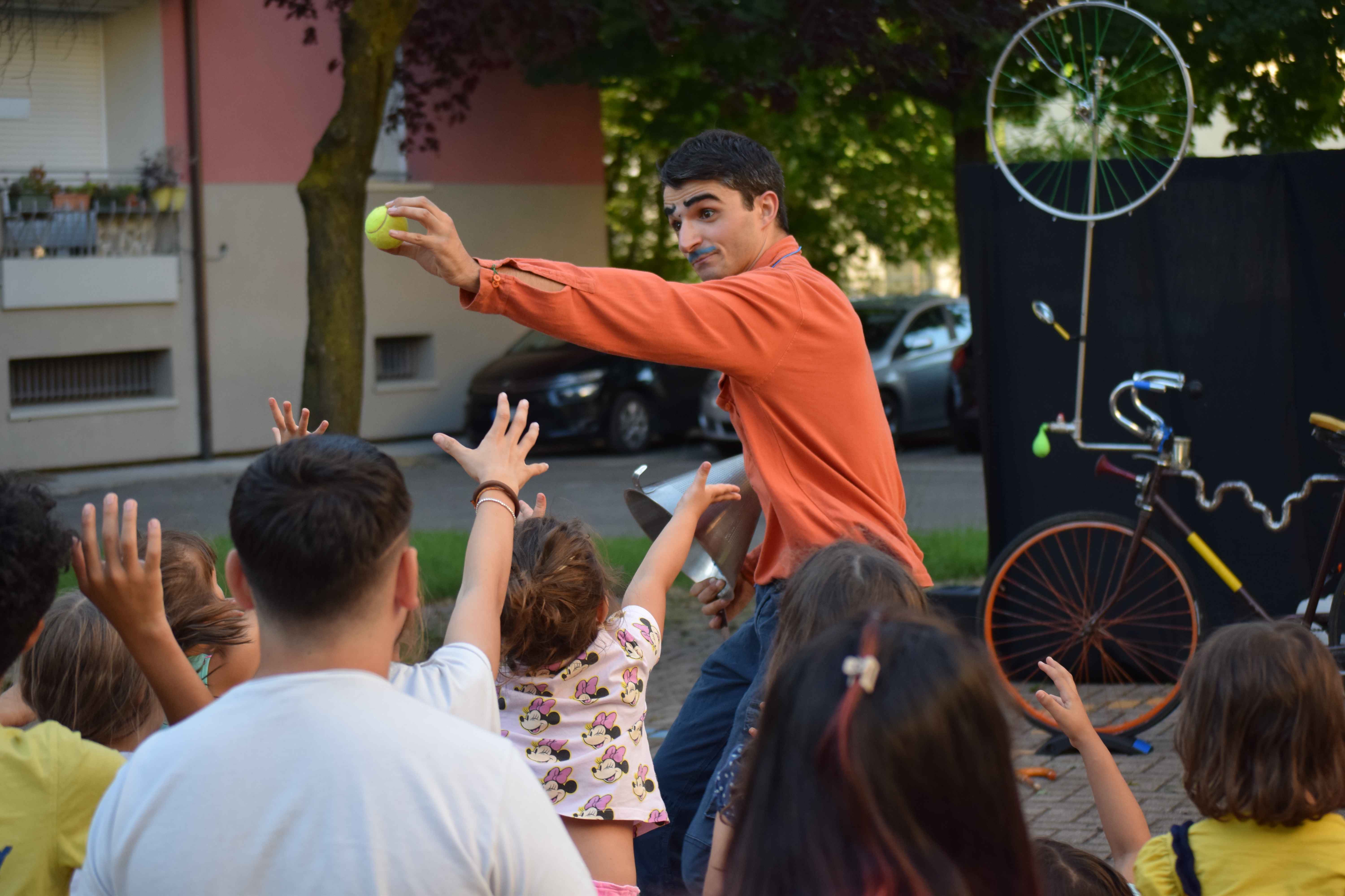 A clown shows a tennis ball to a crowd of children.