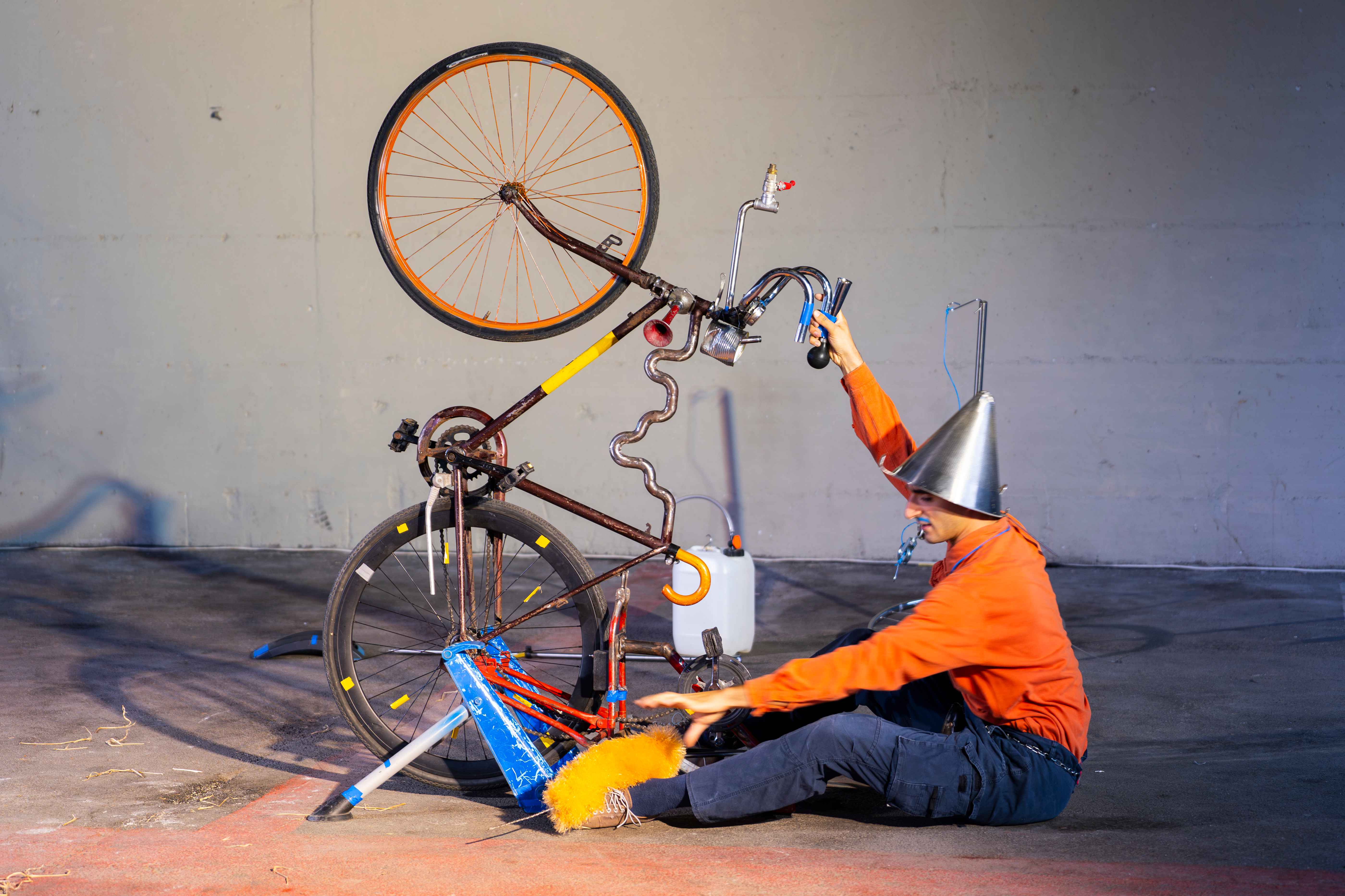 A clown pedals a bike while sitting on the ground.