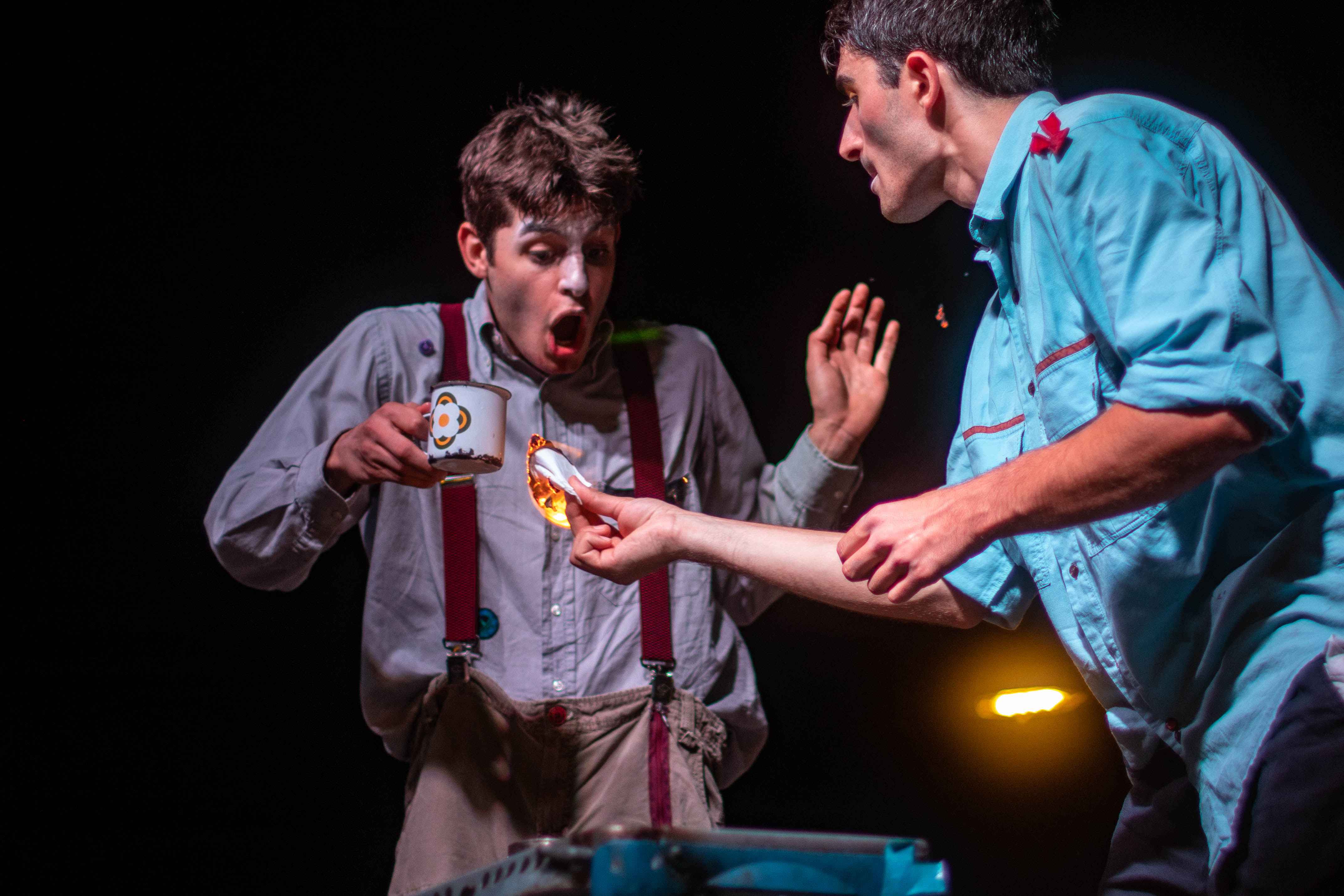 A clown holds a mug and another clown a tissue on fire.