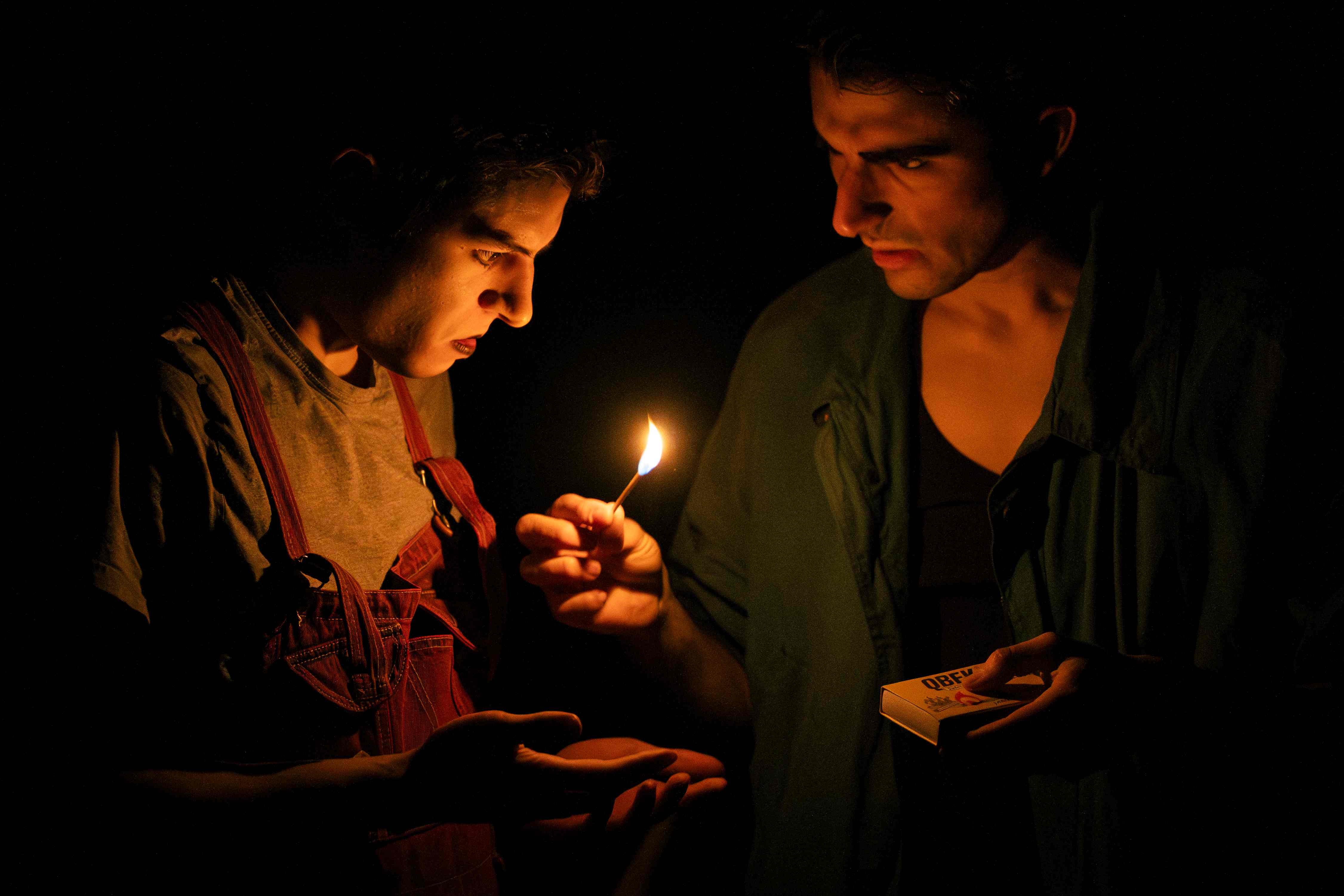 Due clown al buio si illuminano con un fiammifero, uno tiene una scatola di fiammiferi.