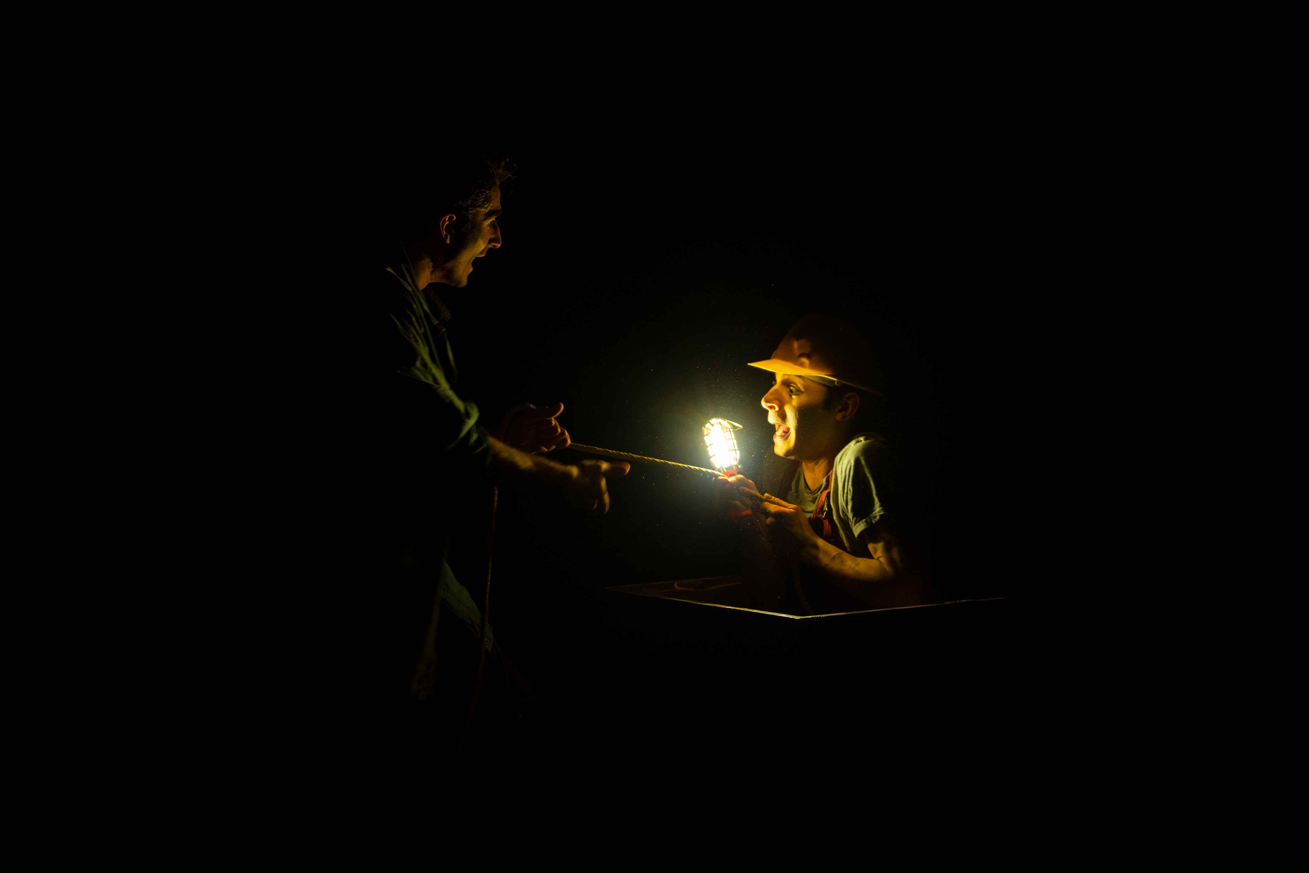 Due clown al buio si illuminano con una lampada da miniera, uno dei due emerge da un carrello con espressione stupita.