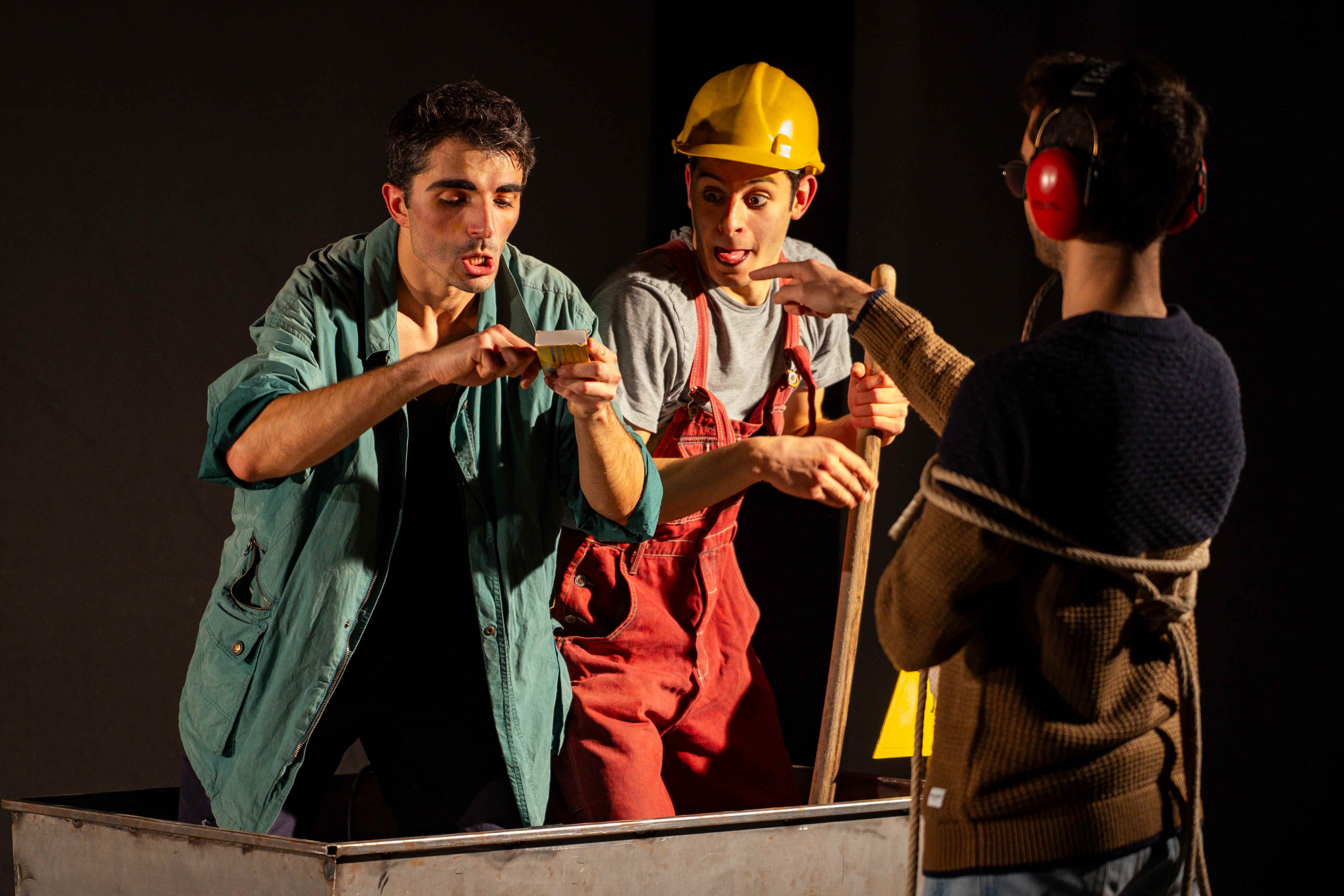 Due clown mostrano stupiti un oggetto trovato a un bambino con le cuffie antirumore, accanto a un carrello da miniera.