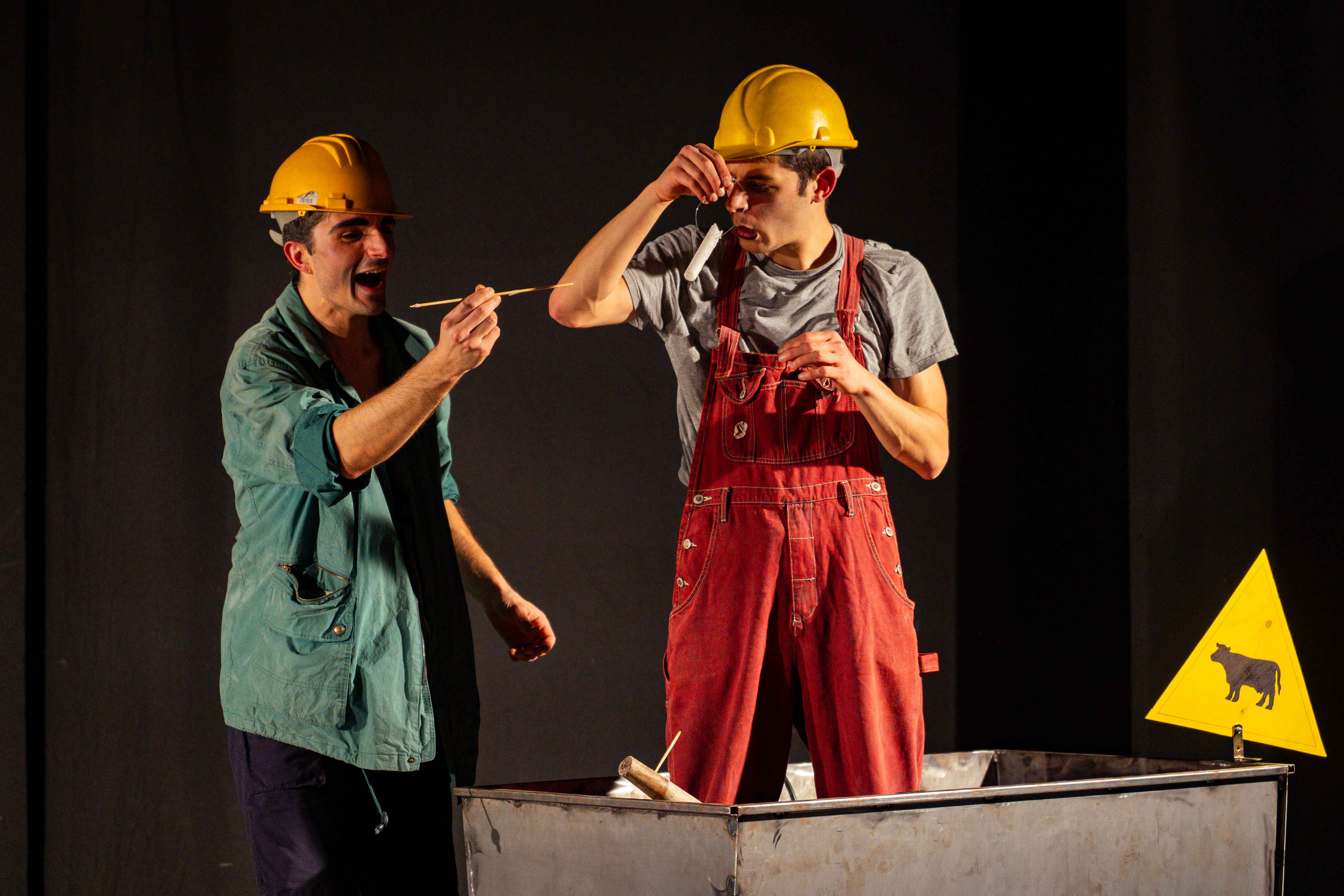 Due clown con caschetti gialli ridono mentre si misurano con un metro a nastro accanto al carrello da miniera.