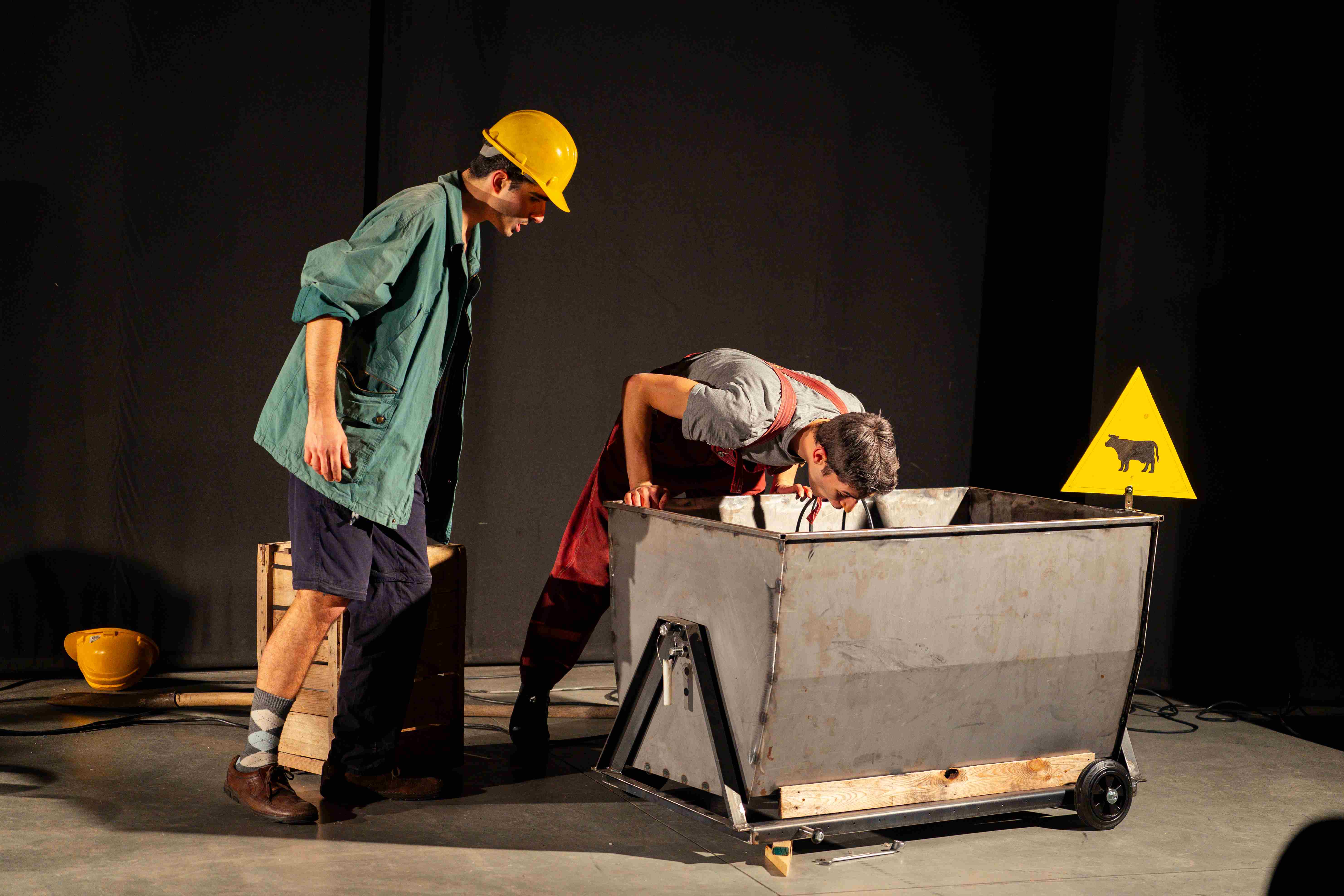 Un clown in giacca verde guarda il compagno in tuta rossa che si sporge dentro un carrello da miniera.
