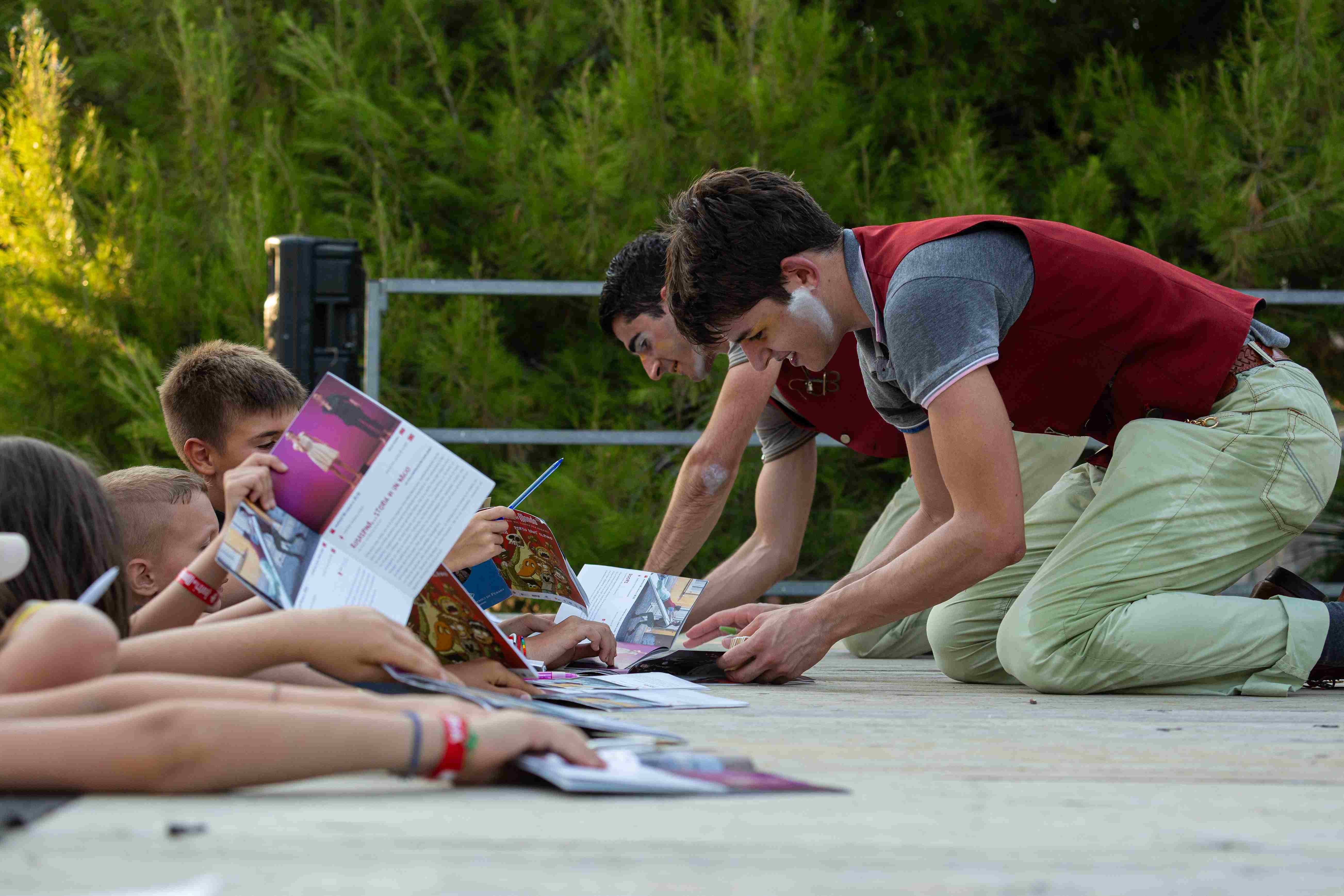 Due attori inginocchiati sul palco fanno autografi ad un gruppo di bambini.