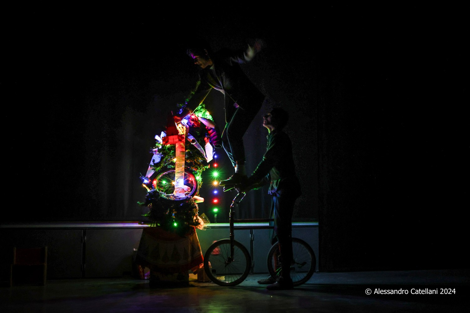 Two clowns on a bike next to an illuminated Christmas tree.