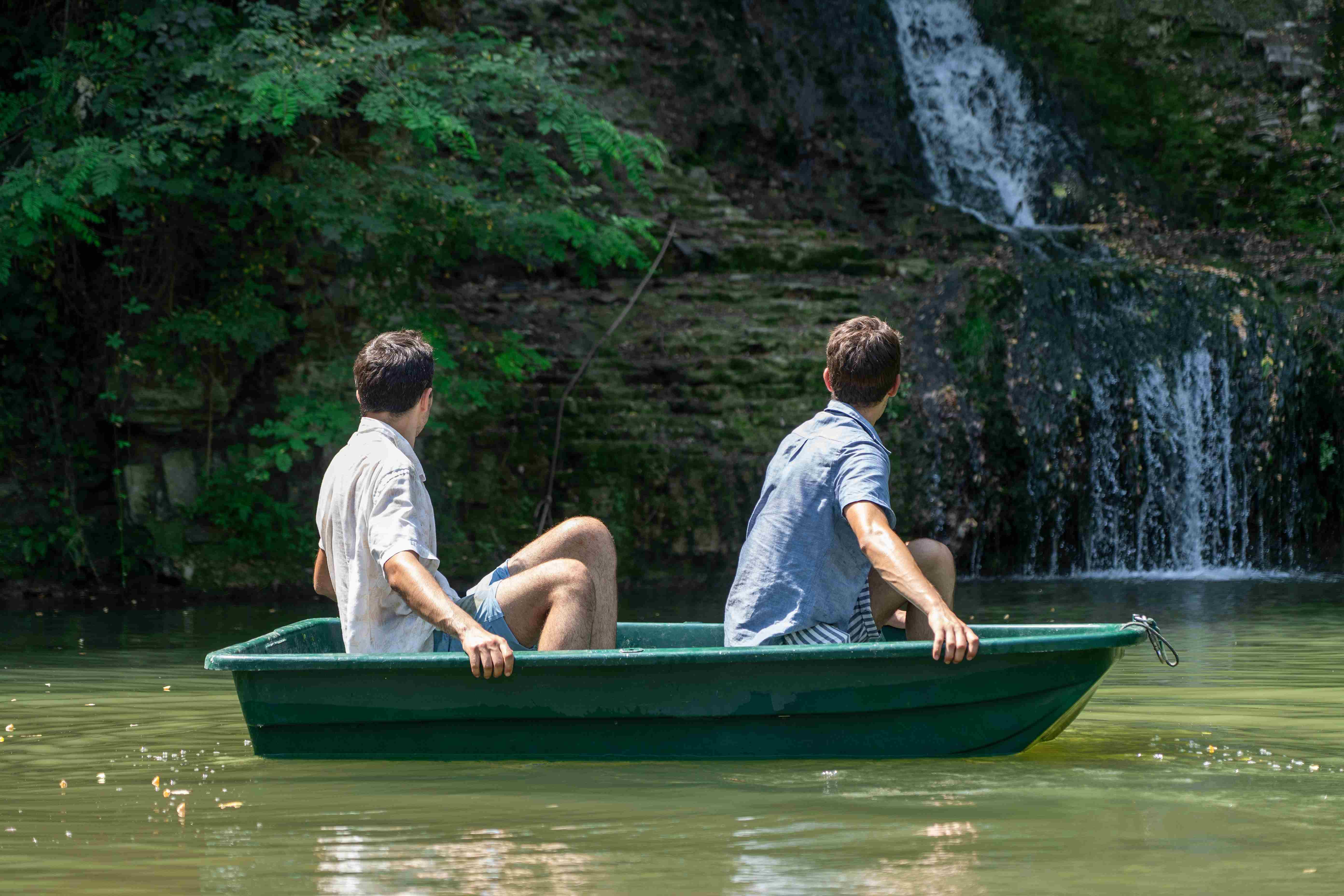 Two characters in a small boat in the middle of a pond look at the waterfall behind them.