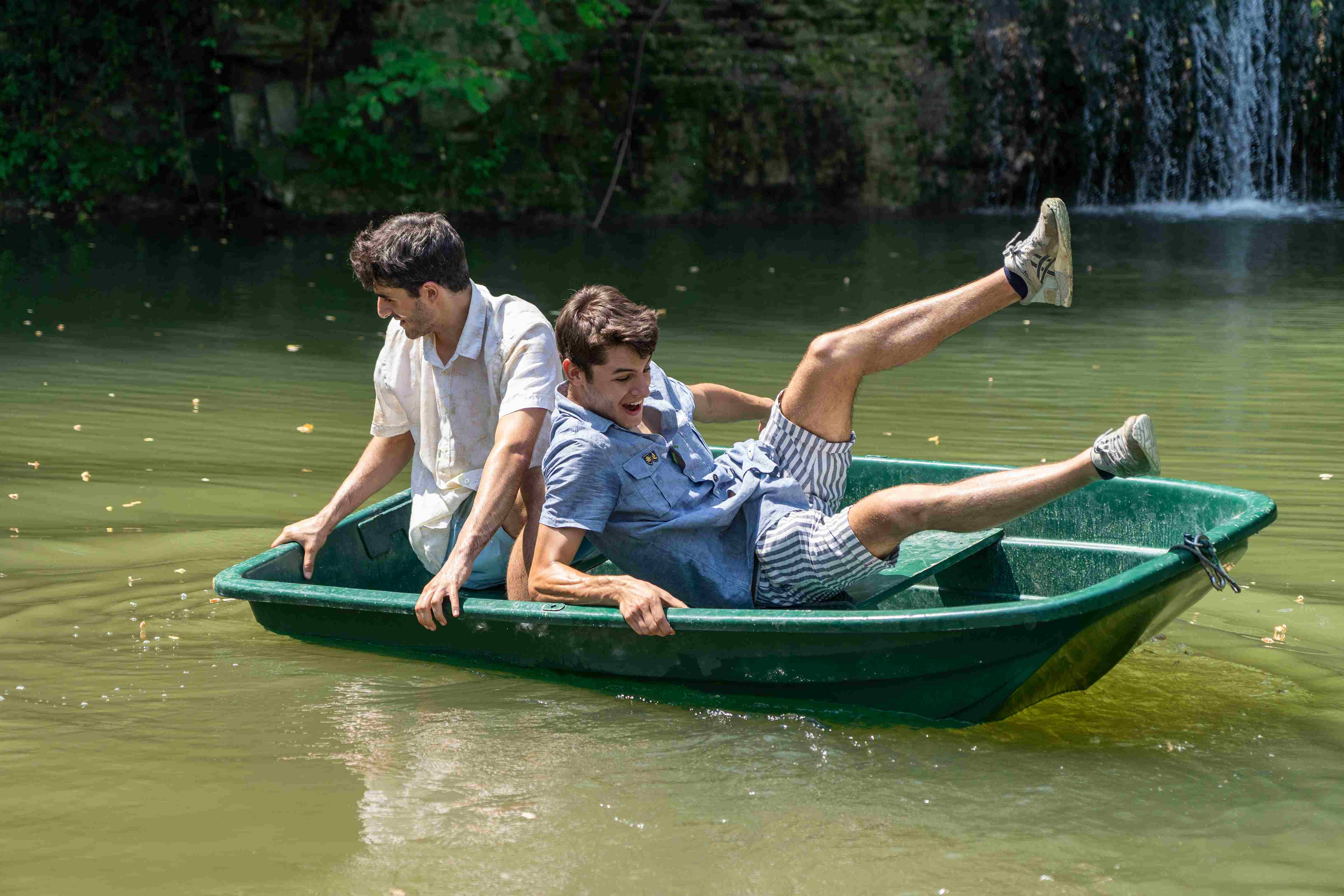 Two people in a green boat in the middle of a pond.