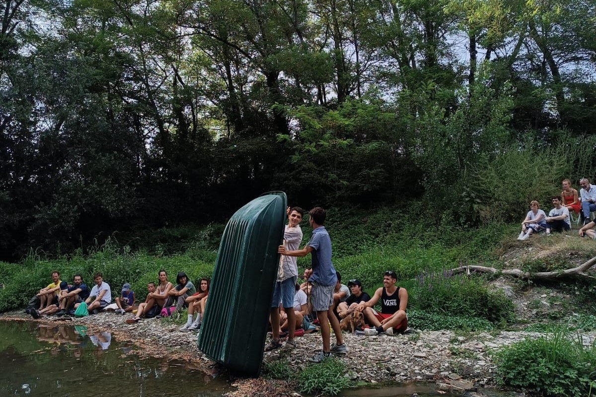 Two clowns on the shore hold up a boat in front of the audience.