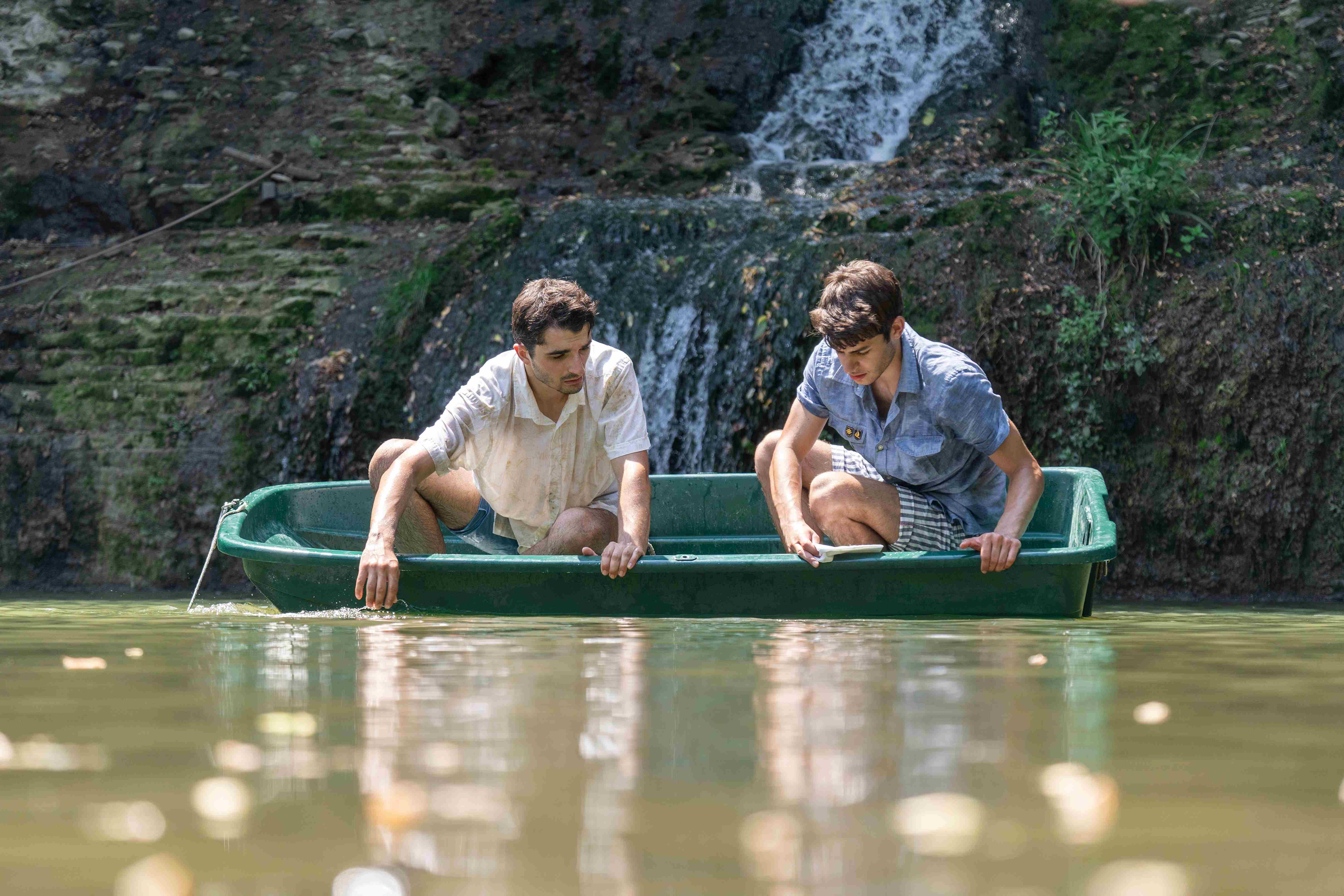 Two clowns in a little green boat with a waterfall behind it watch the reflections in the water.