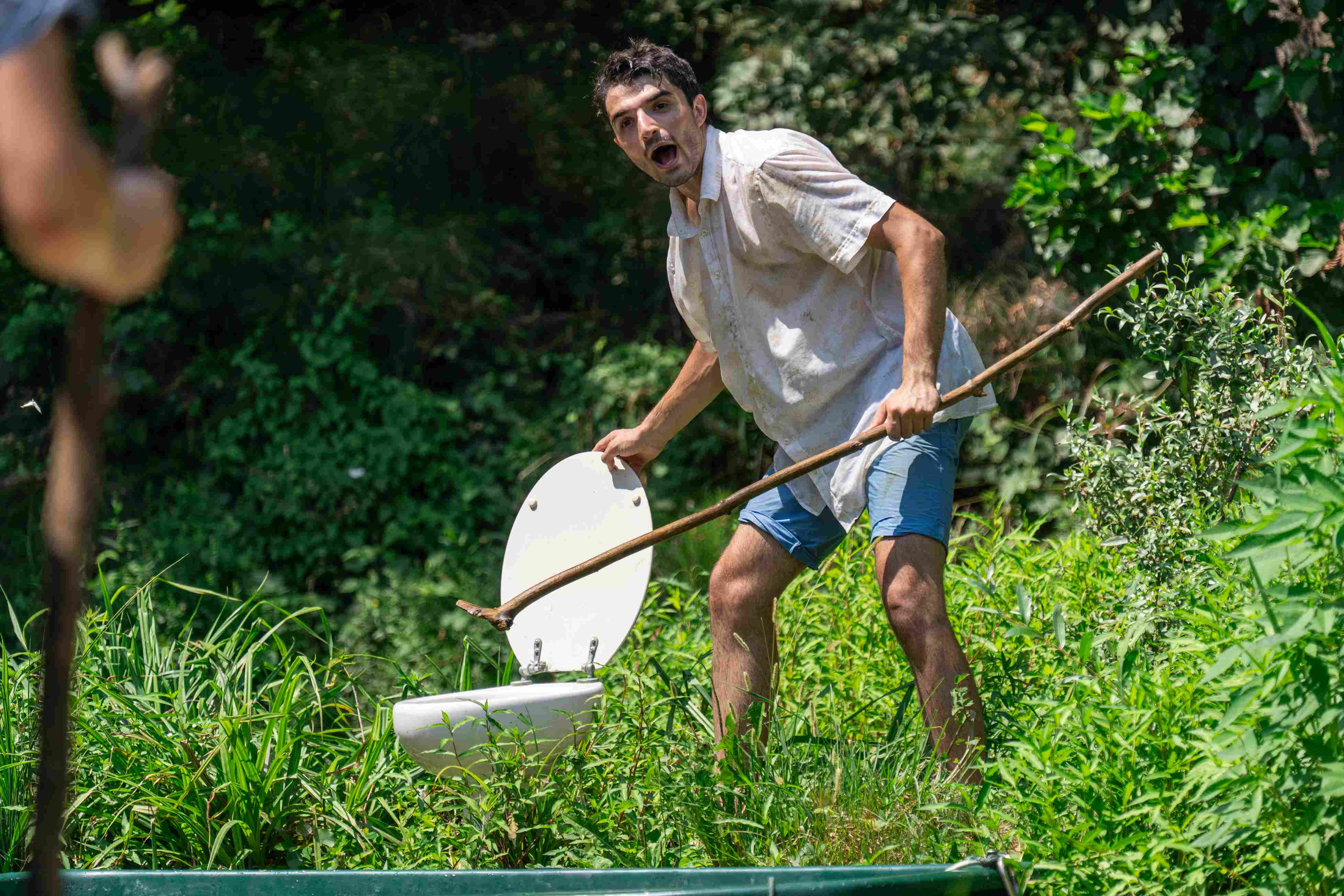 Clown with a stick discovers a toilet in amazement.